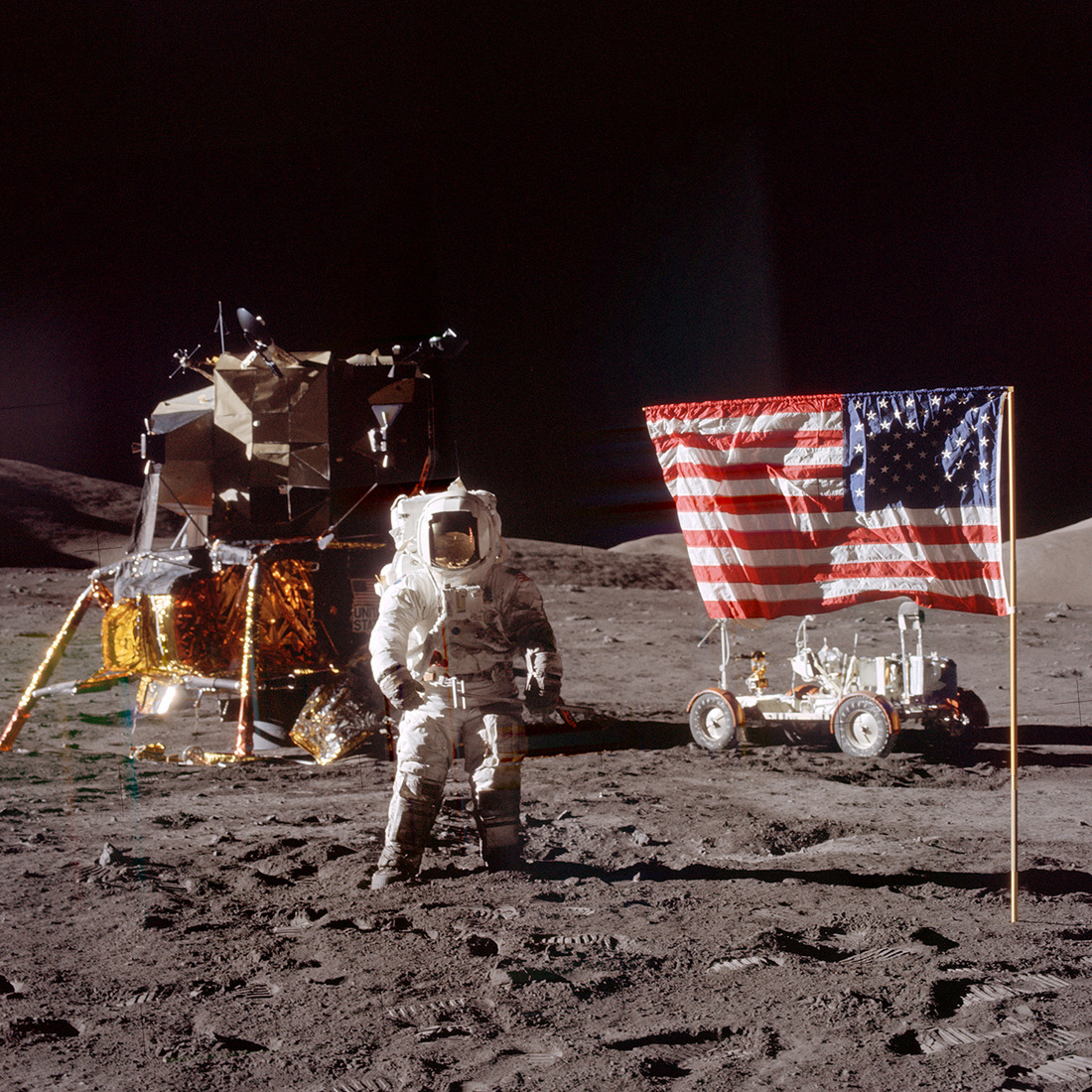 Apollo 17 handheld image of astronaut Jack Schmitt standing to the left of the U.S. flag, with the LM, LRV and the MESA in the background.