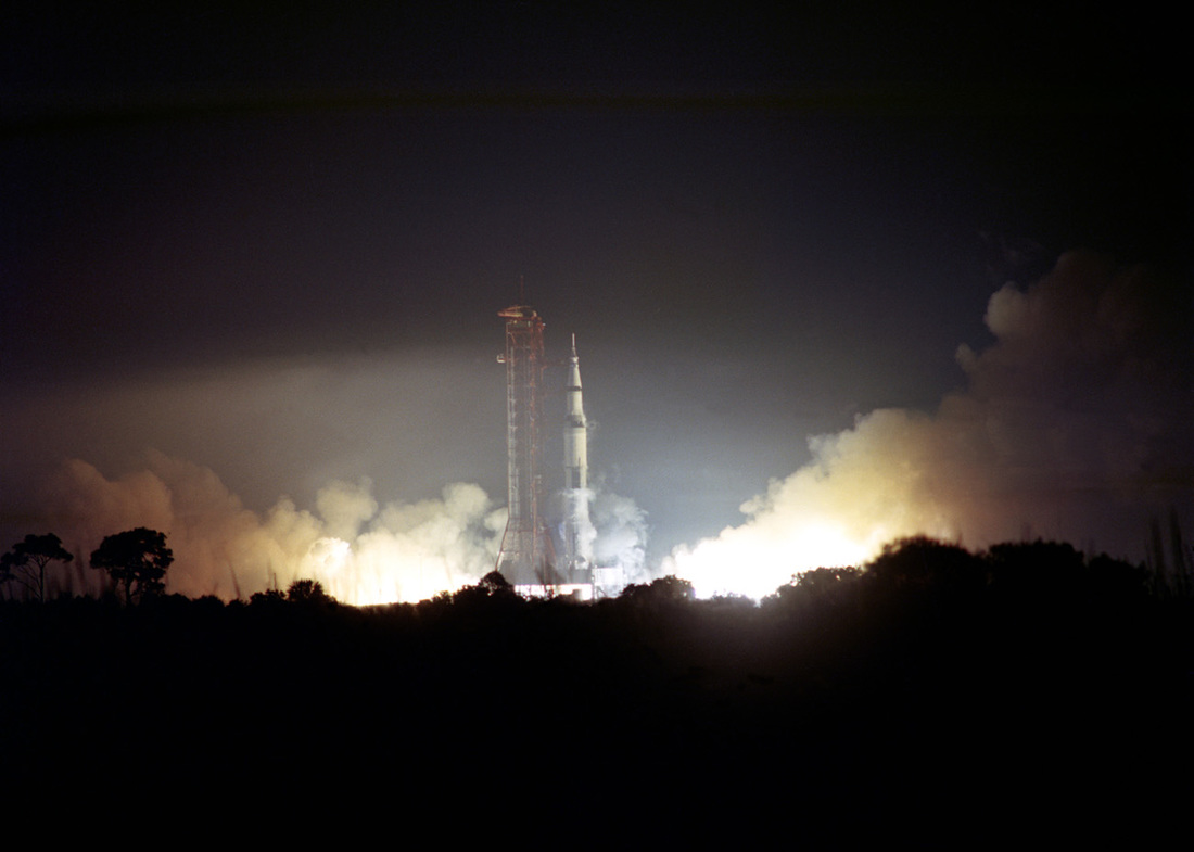 Image of the Apollo 17 space vehicle launching from Kennedy Space Center Space Launch Complex 39A, billowing smoke and flames out either side, lighting up the rocket, gantry, and the Florida night sky..